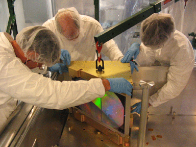 Three people in clean suits touch the APOGEE spectrograph